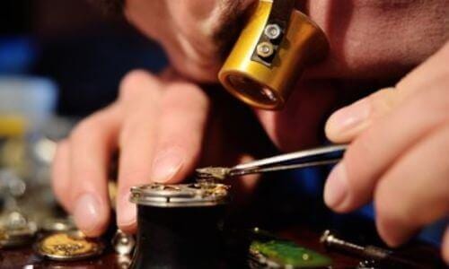orologiaio che con lente ripara il meccanisco di un orologio